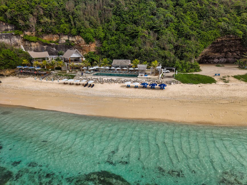 Aerial photo of a picturesque beachfront resort in Bali, showcasing clear waters and lush greenery.