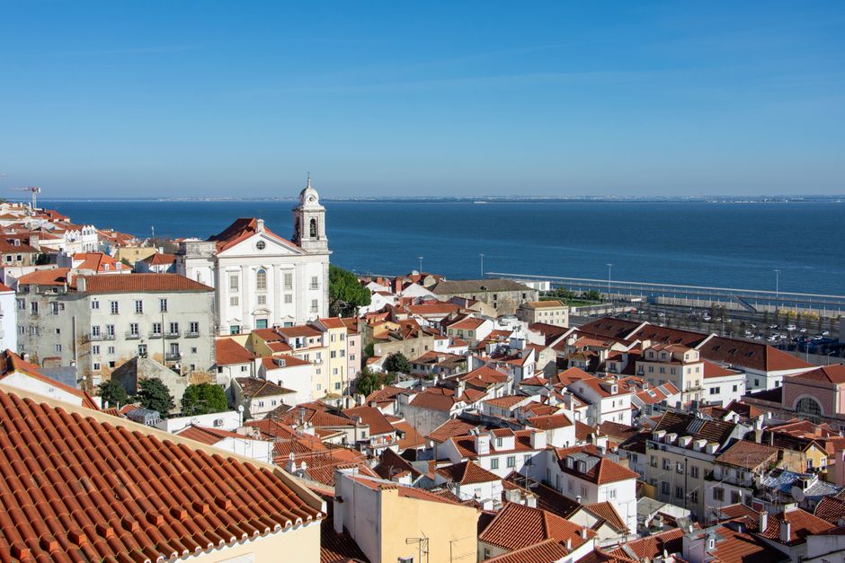 Scenic view of Lisbon's rooftops with a church and river backdrop.