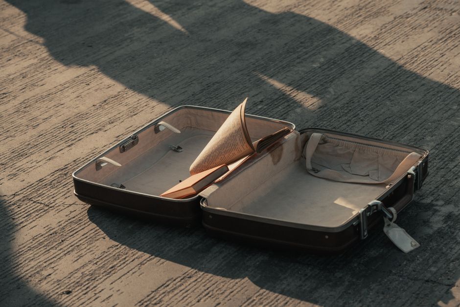 An open suitcase on a pavement with a book inside, casting shadows.