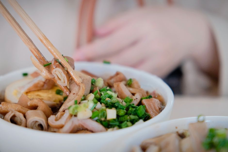 A detailed shot of noodles with green onions held with chopsticks, depicting Asian cuisine.