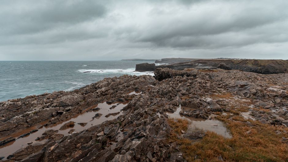 Stunning view of rocky sea cliffs in Ireland under stormy clouds, showcasing nature's raw beauty.