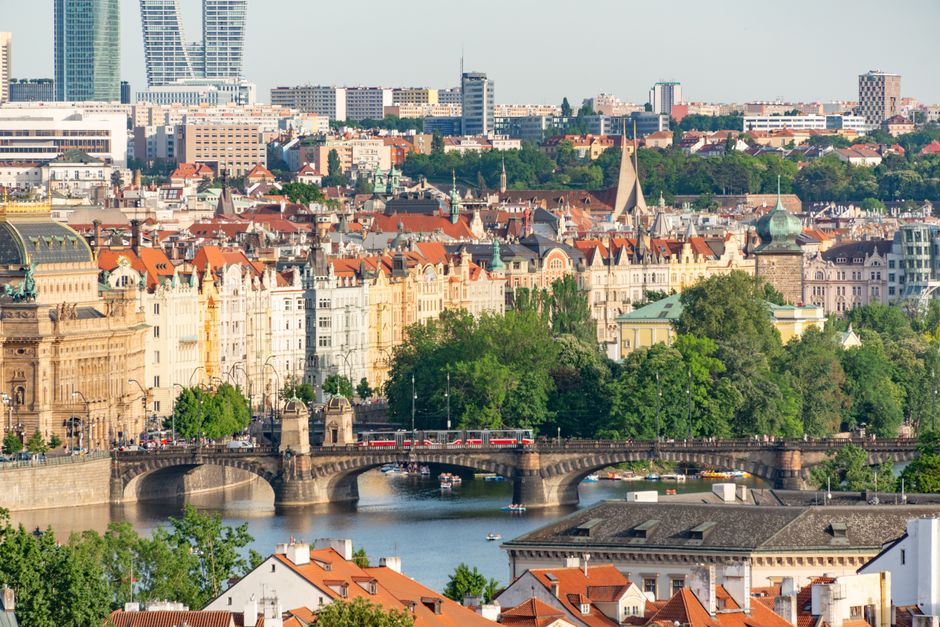 A breathtaking panoramic view of Prague featuring historical buildings, Vltava River, and lush greenery under a bright sky.