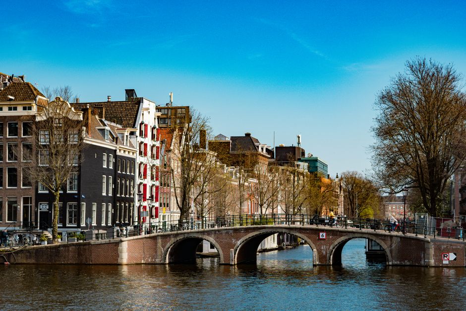 Picturesque view of an Amsterdam canal and bridge with historic buildings and blue sky.