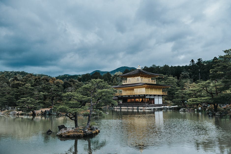 Kinkaku-ji Pavilion in Kyoto, Japan, seen over a serene pond with surrounding forest.