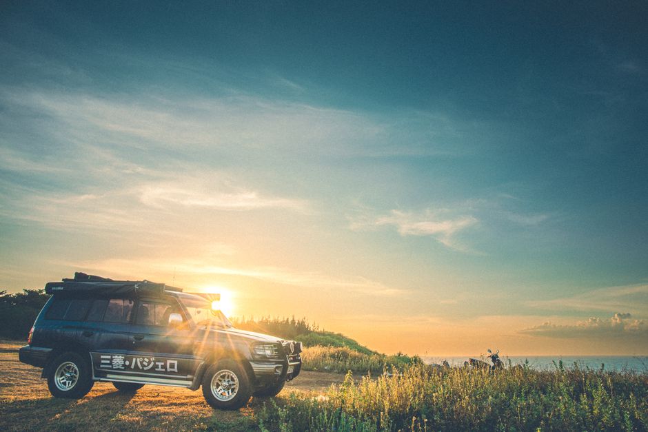 A rugged SUV parked by the ocean during a vibrant sunset in Cửa Tùng, Vietnam.