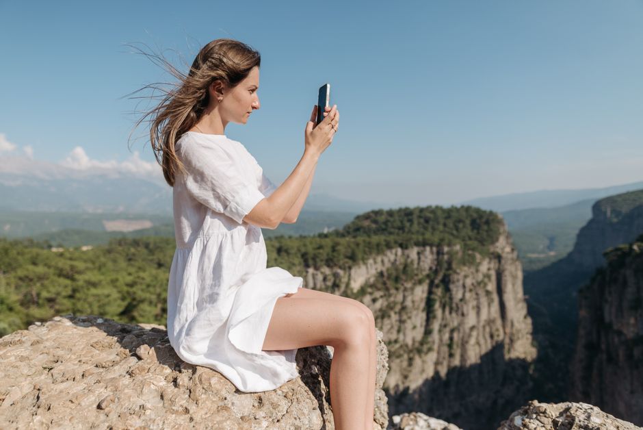 A woman in a white dress sits on a rock capturing a stunning mountain view.
