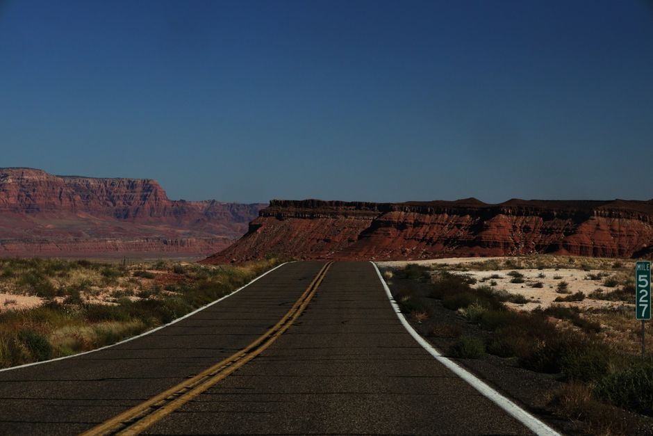 Discover the breathtaking view of a highway cutting through Arizona's iconic red cliffs under a clear blue sky.