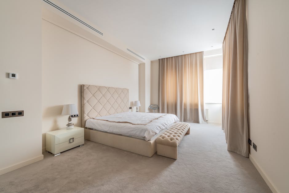 Soft ottoman bench placed near comfortable bed in spacious minimalist bedroom decorated with beige curtains in daylight