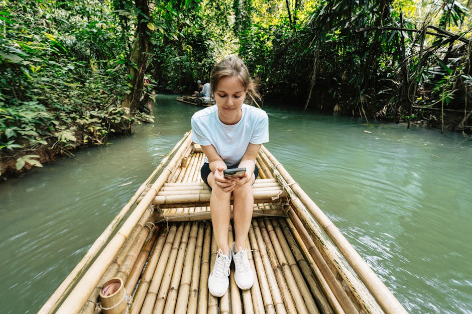 Young woman sitting on a bamboo raft in Krabi, Thailand jungle, using her phone.