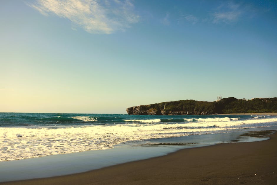 Beautiful sunlit beach in Taiwan with waves lapping against the shore and a scenic cliffside view.