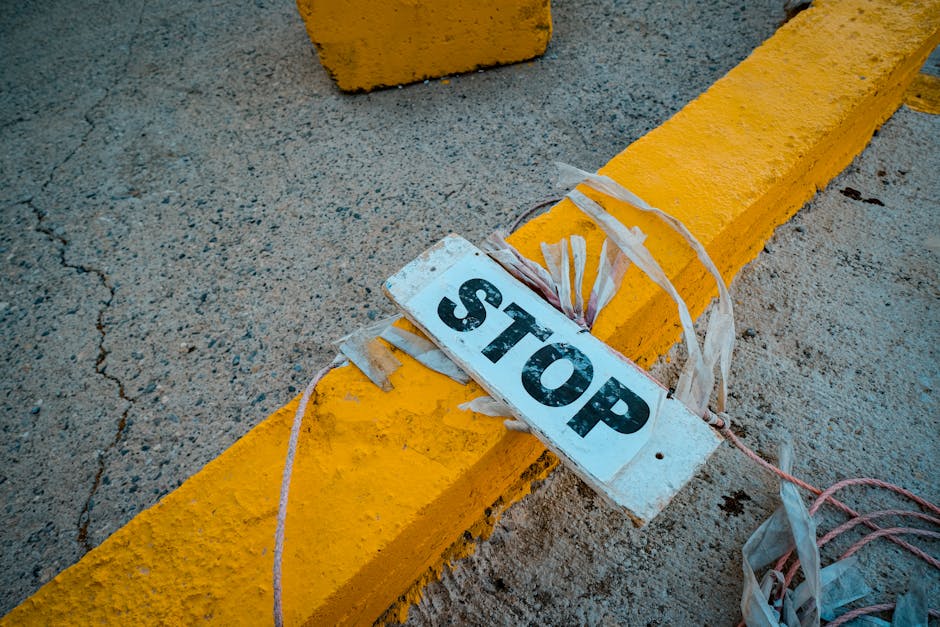 A worn 'STOP' sign placed on a cracked concrete pavement next to a yellow curb.