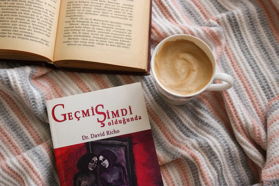 Flat lay of a cozy reading setup with books and a cup of coffee on a striped blanket.